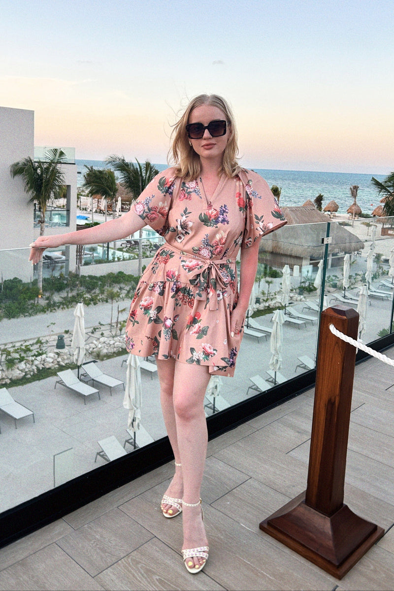 A woman wears a pink floral dress at a tropical beach resort